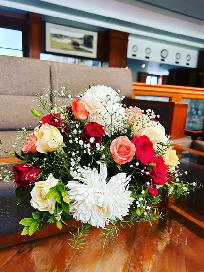 A simple yet elegant floral centerpiece. This arrangement of red, white, and peach roses adds a touch of freshness and color to the guest tables.