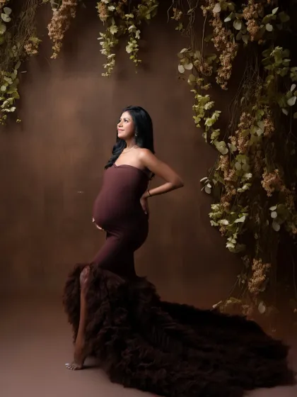 A powerful and elegant pose. The mother-to-be looks statuesque in a brown gown with a ruffled train, set against a backdrop of hanging vines.