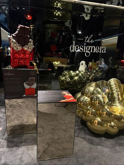 An installation view from our Hyderabad exhibition, featuring the 'Love Chocolate' sculpture and a golden, cloud-like armchair. The mirrored pedestals and dark, reflective walls create an immersive and luxurious atmosphere.