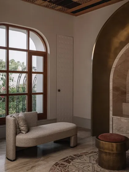 The formal living room at Rehethaan, featuring a ceiling with intricate gypsum embroidery and jewel-like light fixtures. The space also gives a glimpse into the prayer room, with its burnished brass arch and rattan ceiling.