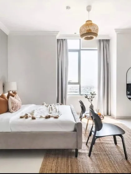 A bright and airy bedroom design that maximizes natural light. The simple color scheme, minimalist furniture, and natural textures like the jute rug and wicker pendant light create a peaceful and relaxing vibe.