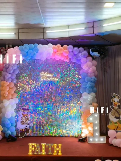 For this first birthday, I created a magical Disney-themed stage. The setup includes a shimmering sequin wall, a multi-colored balloon frame, life-sized cutouts of Disney characters, and personalized light-up marquee letters spelling the child's name.