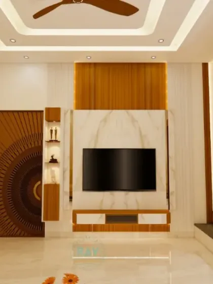 A modern living room featuring a TV unit set against a marble-finish wall, a beautifully carved wooden door, and a view of the adjacent pooja unit.