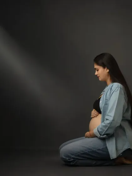 A quiet and contemplative maternity portrait. The simple styling with jeans and a shirt, combined with dramatic lighting, creates a powerful and authentic image focused on the mother's connection with her unborn child.