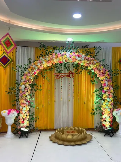 A classic Haldi ceremony setup with a vibrant yellow backdrop, a stunning arch of marigold and rose flowers, and a traditional brass lotus seat for the bride.