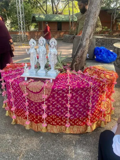 This image shows the altar setup for the Ram Kalash function, featuring the deities placed on a table draped in vibrant pink and gold bandhani fabric. The decor is traditional and respectful for the occasion.