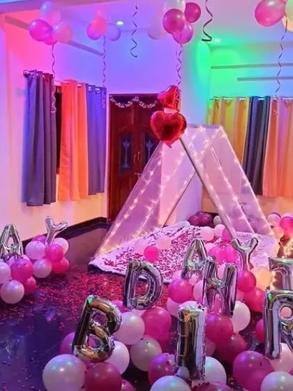 A fun and colorful birthday room decoration. A teepee tent is surrounded by pink balloons and large 'BIRTHDAY' foil letters on the floor.