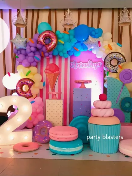 A delicious-looking Candyland theme for a second birthday. The setup is filled with giant props of donuts, macarons, cupcakes, and ice cream, creating a sweet fantasy world.