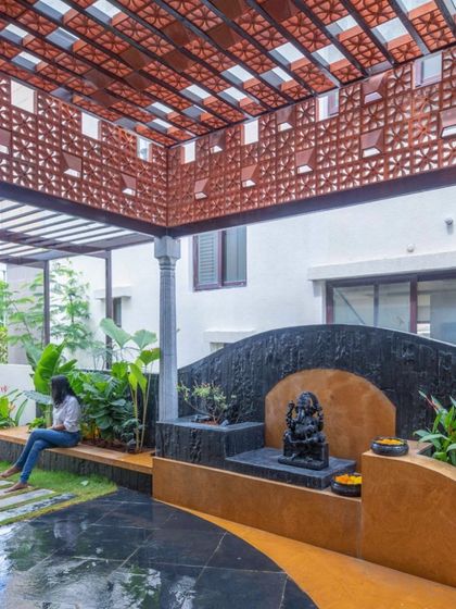 A sacred space designed in a landscaped courtyard. The design uses a mix of materials like stone, terracotta, and concrete to create a textured, earthy backdrop for the Ganesha idol.