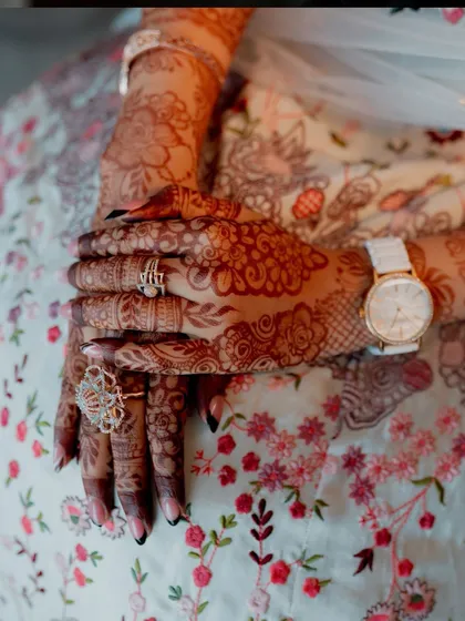 A close-up of the bride's hands, showcasing her intricate mehendi, rings, and watch.