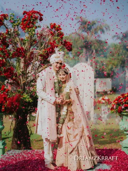 A quiet moment of joy for the couple, showered in petals after their Varmala. The rich red floral trees in the background provided a stunning, natural frame for their portrait.