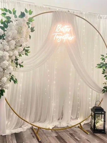 For a modern and elegant engagement or reception, I design stunning backdrops like this one. It features a gold circular frame adorned with lush white flowers, sheer drapes, and a custom 'Better Together' neon sign, all set against a backdrop of twinkling fairy lights.