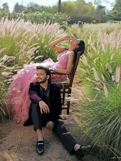 An artistic pre-wedding portrait of a couple in a field of tall, feathery grass. The composition creates a dreamy and romantic atmosphere.