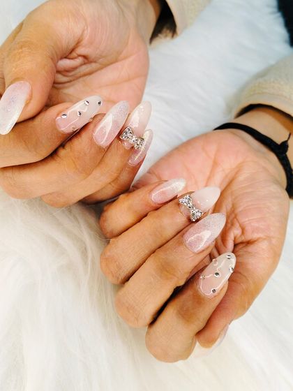 An angelic set of long, almond-shaped extensions with a milky white base, adorned with sparkling rhinestone bows and scattered gems.