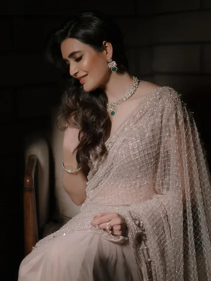Karishma Tanna sitting gracefully, her sparkling saree matched by the brilliance of our contemporary diamond and emerald necklace set.