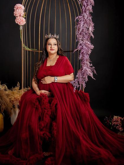 Another angle of the queen-like maternity look, showcasing the rich red gown and the flawless, radiant makeup.