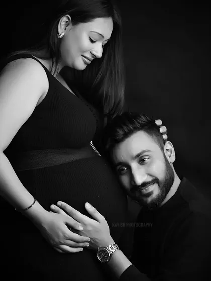 An intimate black and white maternity portrait showing an expecting father listening to the baby bump. This studio shot uses classic lighting to emphasize the emotional connection and anticipation of the couple.