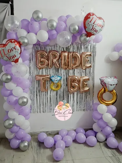 A 'Bride to Be' decoration with a purple and white balloon arch, silver shimmer curtain, and 'I Love You' foil balloons.