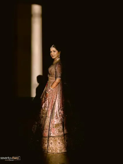 A bride stands in a dark room, illuminated by a single column of light, creating a dramatic and elegant silhouette.
