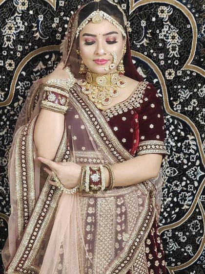 A bride wearing a deep maroon velvet lehenga with gold embroidery. The soft pink dupatta provides a lovely contrast.