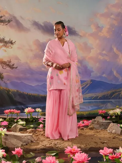 A full-length shot of a pink sharara set from the Gulnaar collection, set against a dreamy, painted backdrop.