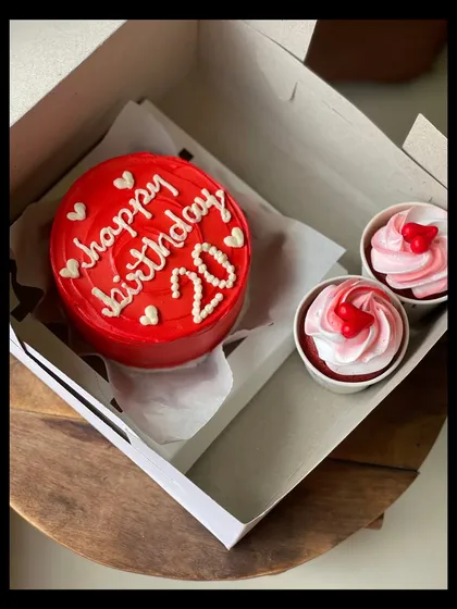 A vibrant red bento cake for a 20th birthday, paired with two pretty pink and white swirled cupcakes. The tiny hearts on all the treats make it an extra sweet gift.