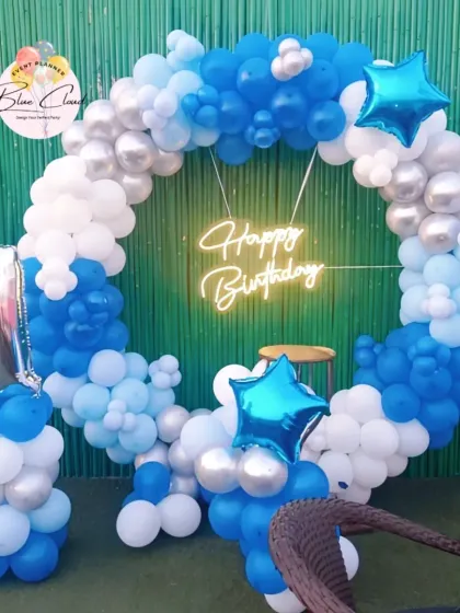 A first birthday balloon ring in shades of blue, white, and silver with a neon sign.