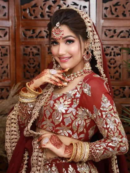 A bright and happy bride in a red and gold lehenga. The makeup is fresh and radiant, with a focus on a beaming smile.