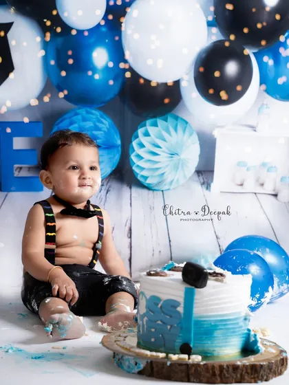 A "Boss Baby" themed cakesmash featuring a little boy looking dapper in a bow tie and suspenders, curiously exploring his blue and white cake.