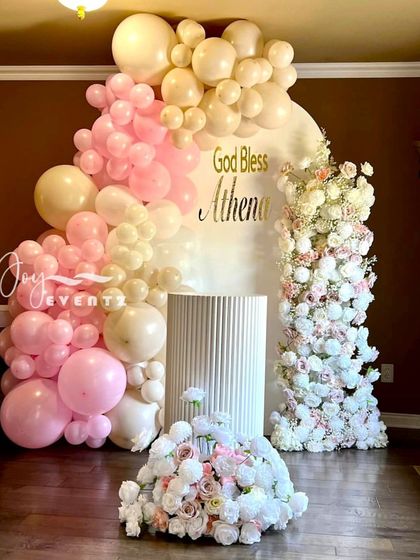 A lovely pastel balloon and floral decoration for a baptism. The arrangement in shades of pink and cream frames a custom "God Bless" backdrop, creating a soft and celebratory atmosphere.