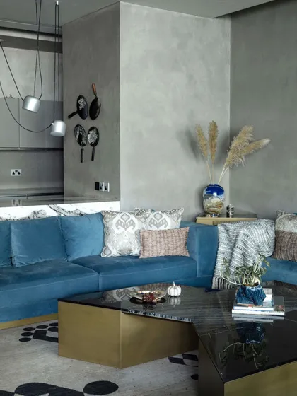 The family lounge at the Bammi Residence, featuring a custom coffee table and a plush blue sectional sofa. Whimsical art pieces depicting utensils add a playful touch to the breakfast counter area.