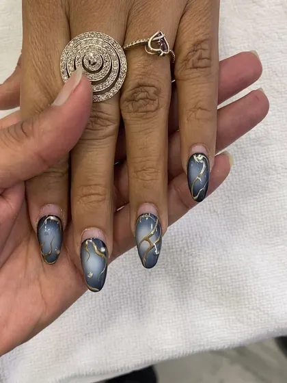 A beautiful example of airbrush nails with a blue-grey gradient, gold chrome accents, and a marble-like effect.