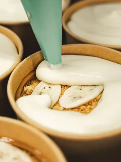 A behind-the-scenes look at our Banoffee Pie being made, with fresh banana slices being layered over a biscuit base.