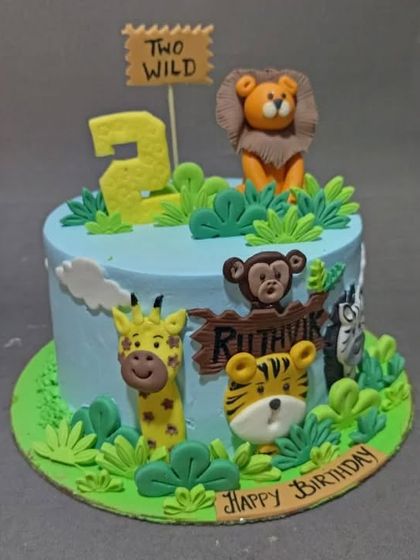 A "Two Wild" birthday cake with a jungle theme. This cake features several cute, hand-sculpted animals like a lion, monkey, and tiger, perfect for a second birthday.