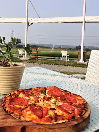 A freshly baked pepperoni pizza on our outdoor patio table, with the sunny driving range in the background.