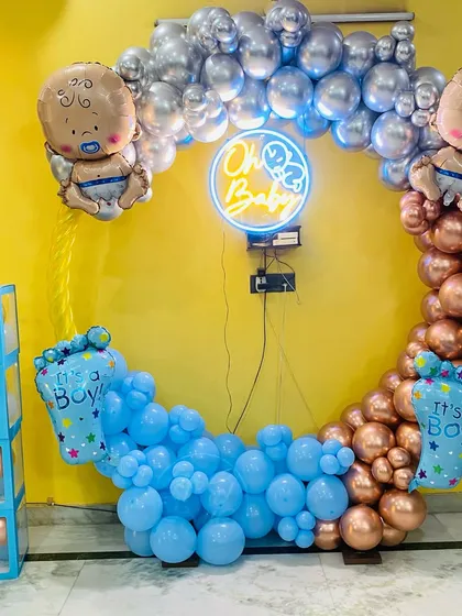An "Oh Baby" themed decoration for a baby boy. The setup includes a balloon ring in blue, silver, and rose gold, with "It's a Boy" foil balloons and transparent "BABY" boxes.