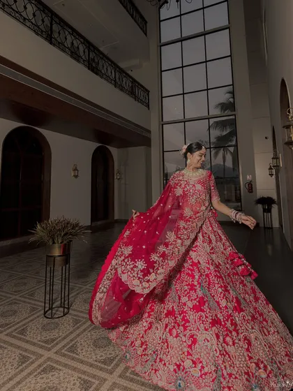 A bride in her magnificent red lehenga, captured in a way that shows off the full splendor of her outfit. The movement in the fabric adds a dynamic quality.