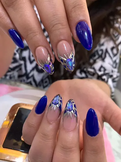 A bold and royal design featuring cobalt blue nails with intricate silver and iridescent crystal embellishments.