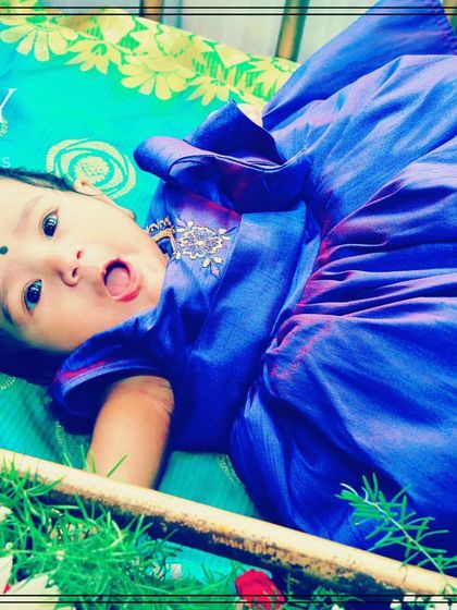 A cute shot of a baby dressed in a lovely blue frock, enjoying the comfort of the decorated cradle.