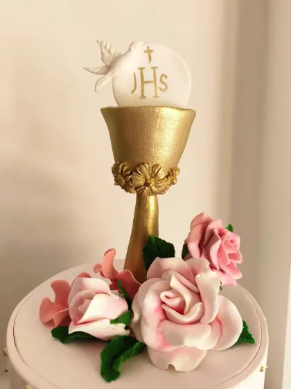 A close-up of the First Holy Communion cake, showing the detailed golden chalice and the handcrafted pink sugar roses.