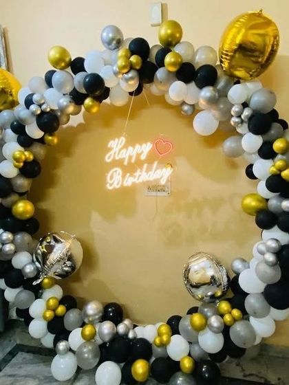 A circular balloon photo frame in black, white, silver, and gold, complete with a "Happy Birthday" neon sign.
