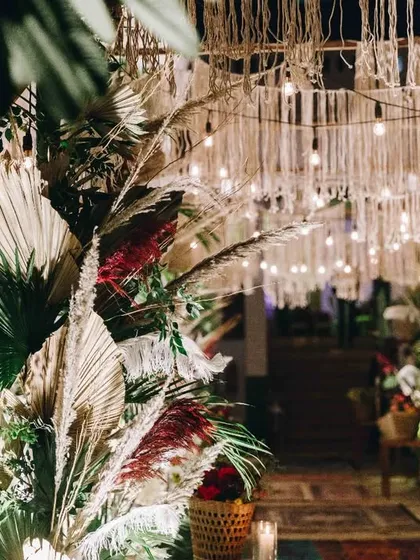 The entrance to the boho-themed Sangeet, with a macrame curtain and an aisle of layered rugs. The design combines natural textures with warm, inviting light.