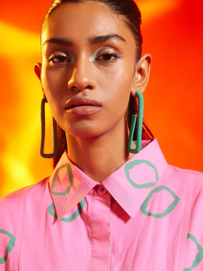 A close-up beauty shot from a campaign for Nakateki. The styling pairs a brightly colored shirt with oversized green earrings, creating a bold and playful color story.