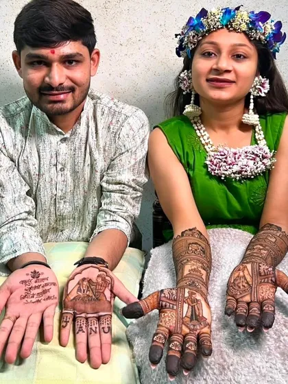 A lovely photo of a couple showing their personalized mehndi. The bride has a full bridal design, while the groom has her name and a mantra on his palm.