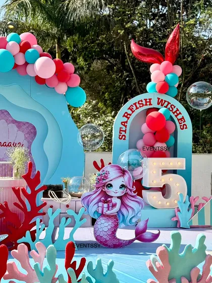 An adorable mermaid-themed party with an "Under the Sea" backdrop. The setup includes a "Starfish Wishes" arch, a cute mermaid cutout, coral props, and a marquee number "5" for the birthday girl.