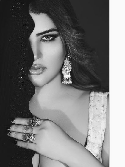 A powerful black and white close-up, using a dark fabric to frame one side of the face. This creates a high-contrast, artistic beauty shot that emphasizes the eyes and jewelry.