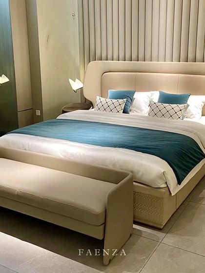 This bedroom is a study in neutral-toned luxury. The bed features a unique woven detail on the frame and is paired with a matching bench. The fluted wall paneling behind adds texture and depth.