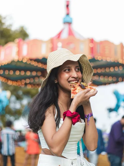 Pizza and festivals are a perfect match. Here's a guest enjoying a slice at Zomaland, with a carousel in the background adding to the fun atmosphere.