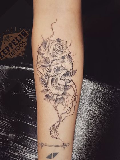 A skull and rose tattoo, symbolizing the duality of life and death, beauty and decay. The design is rendered in a fine-line, illustrative style.