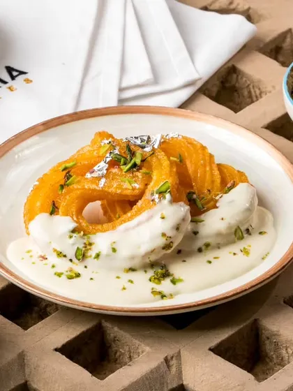 A dessert that perfectly captures our spirit of innovation. This is our signature Paneer Jalebi, served on a bed of rich, creamy rabri and garnished with pistachios. It's a unique sweet ending your guests will talk about for years.